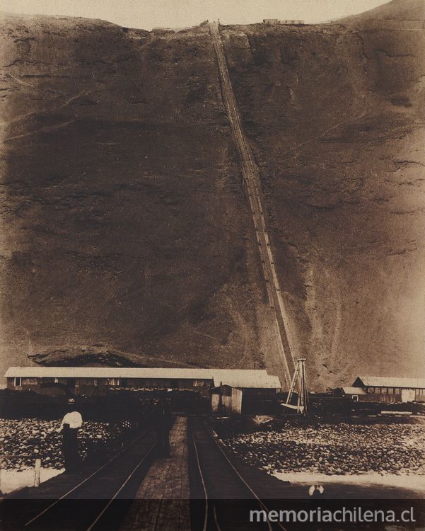 Pie de página: Caleta Buena. Andarivel, Bodega y Muelle perteneciente a la Oficina Salitrera Agua Santa. 1889. Fotografía de L. Boudat.