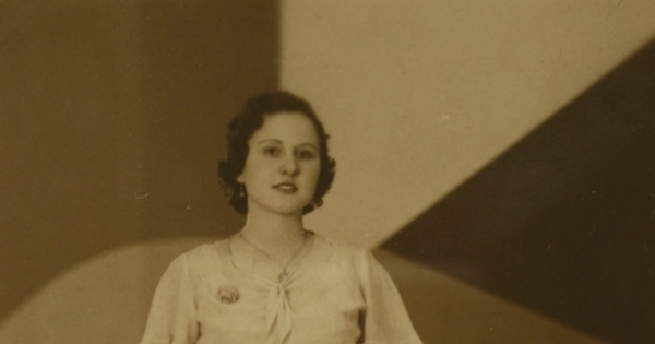 Mujer posando de pie, con un vestido entallado, amarrado en la cintura, entre 1940 y 1950