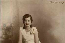 Adolescente de vestido blanco largo adornado con broderí en la parte inferior sentada en un piso de madera sobre alfombra, entre 1930 y 1940
