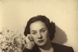 Mujer joven sentada y apoyada sobre un mueble con un jarro de flores, entre 1930 y 1940