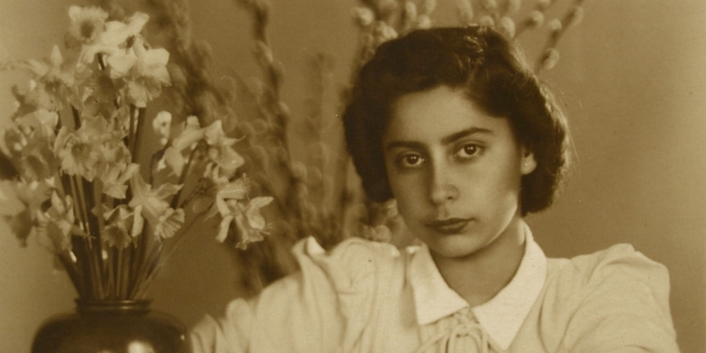 Mujer joven, vestida de verano y apoyada en un mueble: en frente tiene un macetero con flores blancas y a sus espaldas se ve unos brotes de ramas largas, entre 1940 y 1950