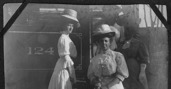 Cuatro señoras, con sombreros, posan en la escalera del tren, portan sombrillas