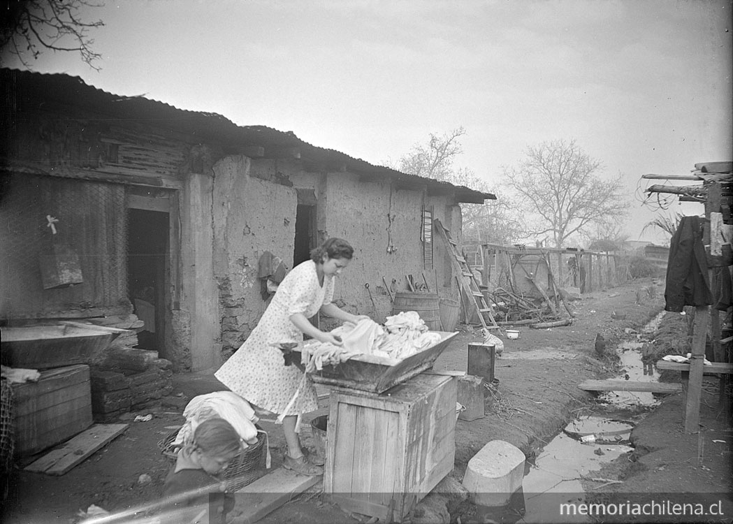 Mujer lavando un alto de ropa en la arteza en el patio de la casa