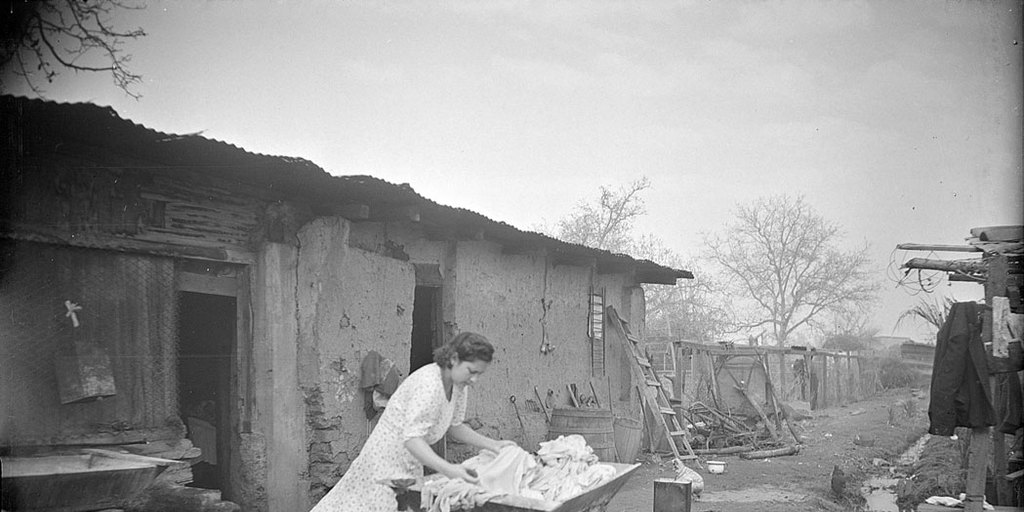 Mujer lavando un alto de ropa en la arteza en el patio de la casa