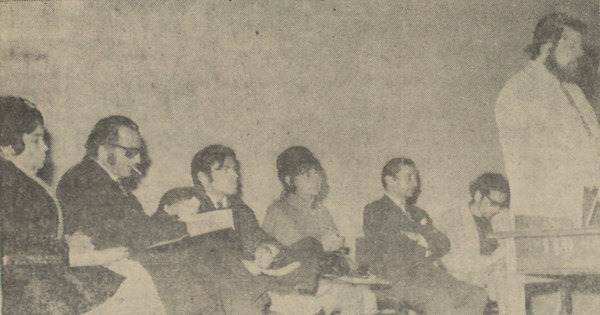 Oliver Welden de pie leyendo y Alicia Galaz sentada junto a grupo de escritores