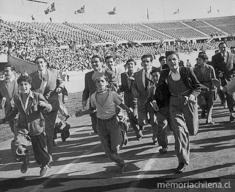 Pie de foto: Hinchas de fútbol corren por la pista de ceniza del Estadio Nacional, 1948