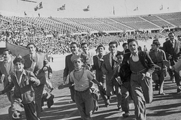 Pie de foto: Hinchas de fútbol corren por la pista de ceniza del Estadio Nacional, 1948