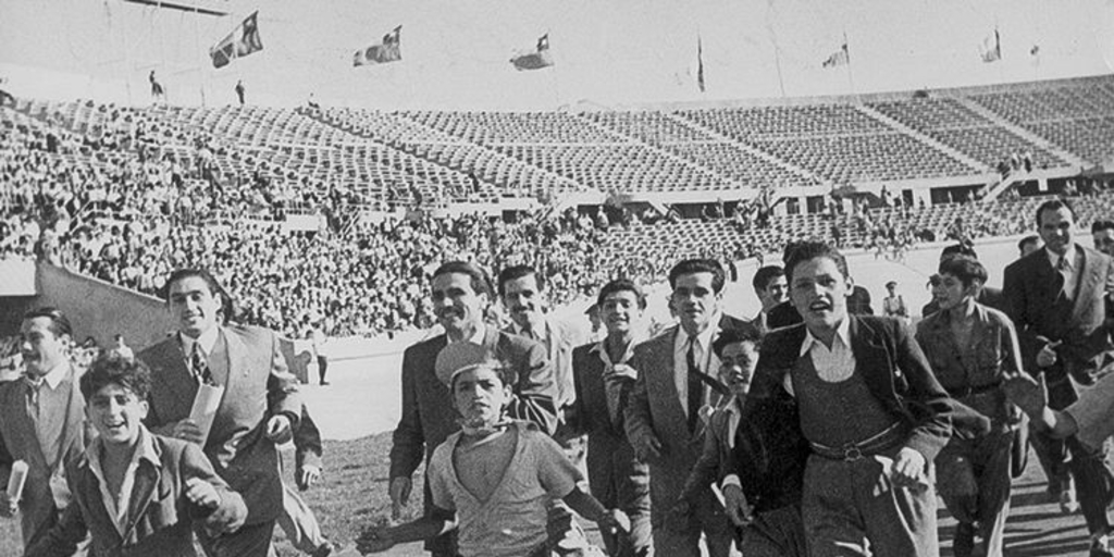 Pie de foto: Hinchas de fútbol corren por la pista de ceniza del Estadio Nacional, 1948