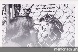 Pie de foto: Día de visita de prisioneros en el Estadio Nacional, 1973. En Cozzi, Adolfo. Estadio Nacional. Santiago: Edit. Sudamericana, 2000. 108 p. Página sin número. Octava foto desde pág. 100, sin pie de foto. Imagen de beso a través de la reja.