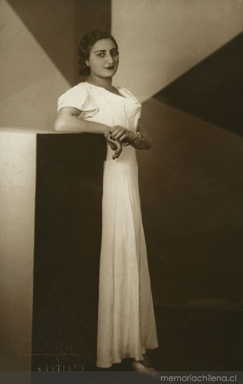 Mujer joven con rasgos árabes, está de pie, con vestido largo de manga corta color blanco, entre 1940 y 1950