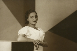 Mujer joven con rasgos árabes, está de pie, con vestido largo de manga corta color blanco, entre 1940 y 1950