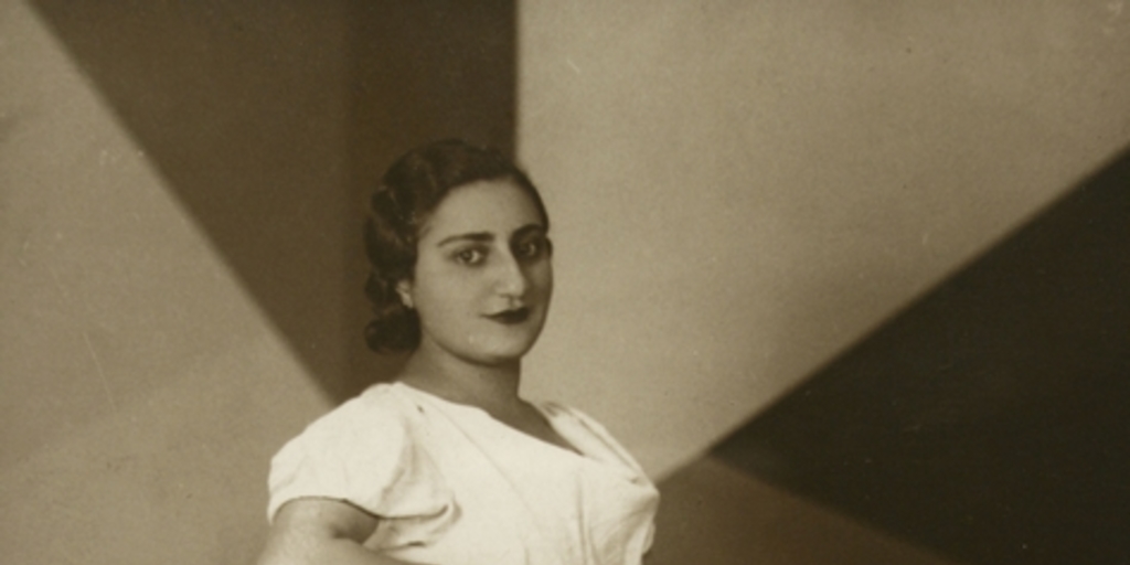 Mujer joven con rasgos árabes, está de pie, con vestido largo de manga corta color blanco, entre 1940 y 1950