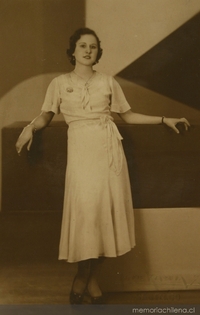 Mujer posando de pie, con un vestido entallado, amarrado en la cintura, entre 1940 y 1950
