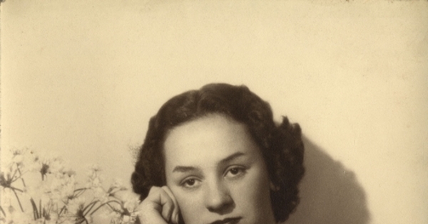 Mujer joven sentada y apoyada sobre un mueble con un jarro de flores, entre 1930 y 1940