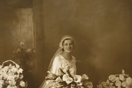 Mujer vestida de novia con dos ramos grandes de flores a su alrededor y un ramo pequeño en sus manos, entre 1928 y 1930